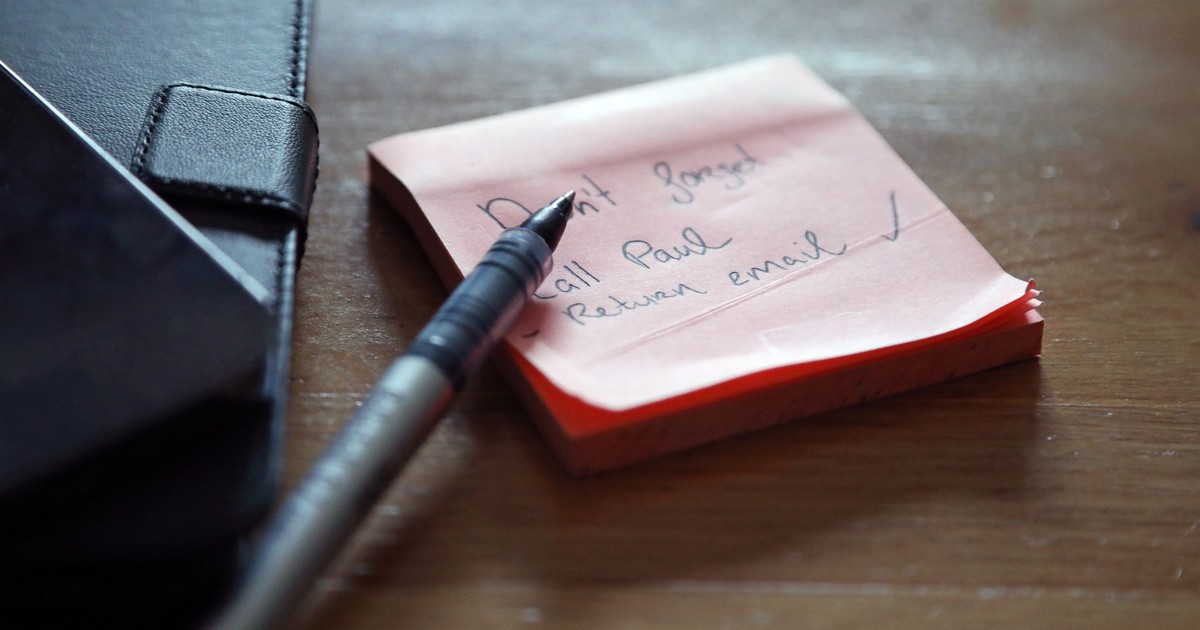 A close-up of sticky notes with a to-do list, a pen, and a wallet on a wooden desk.