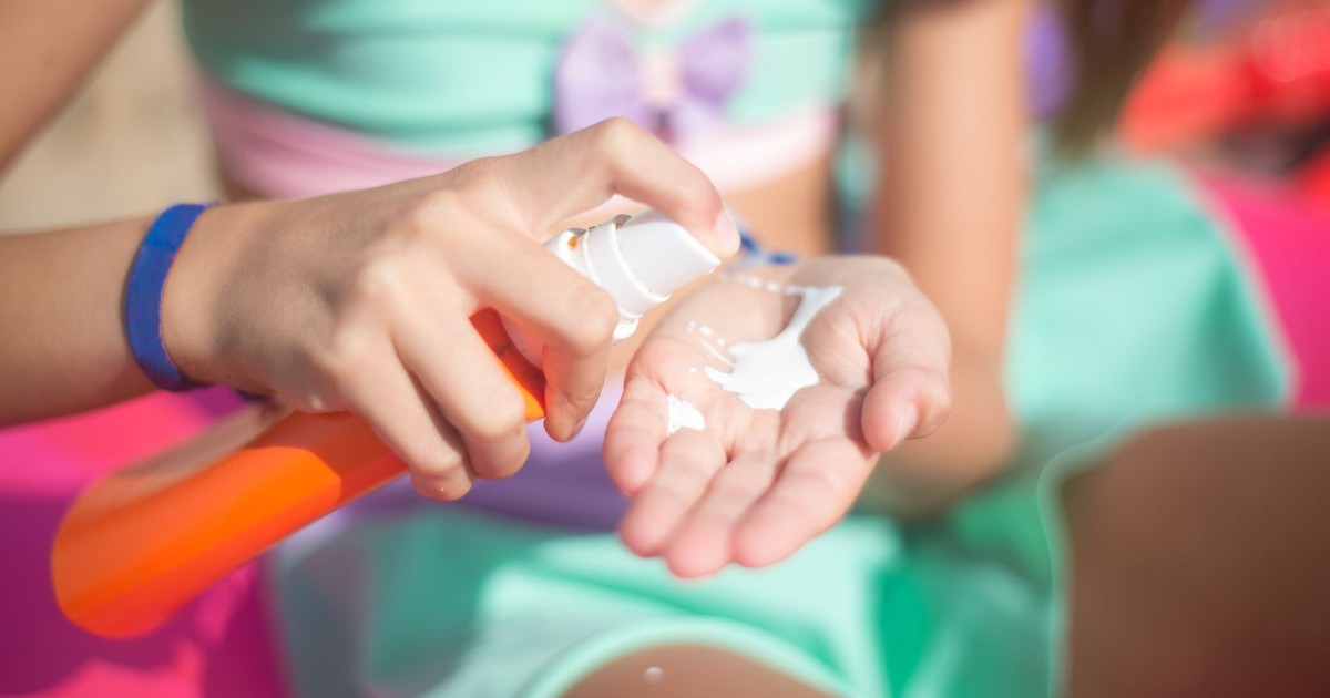 Young girl applying sunscreen from spray bottle outdoors. Summer protection.
