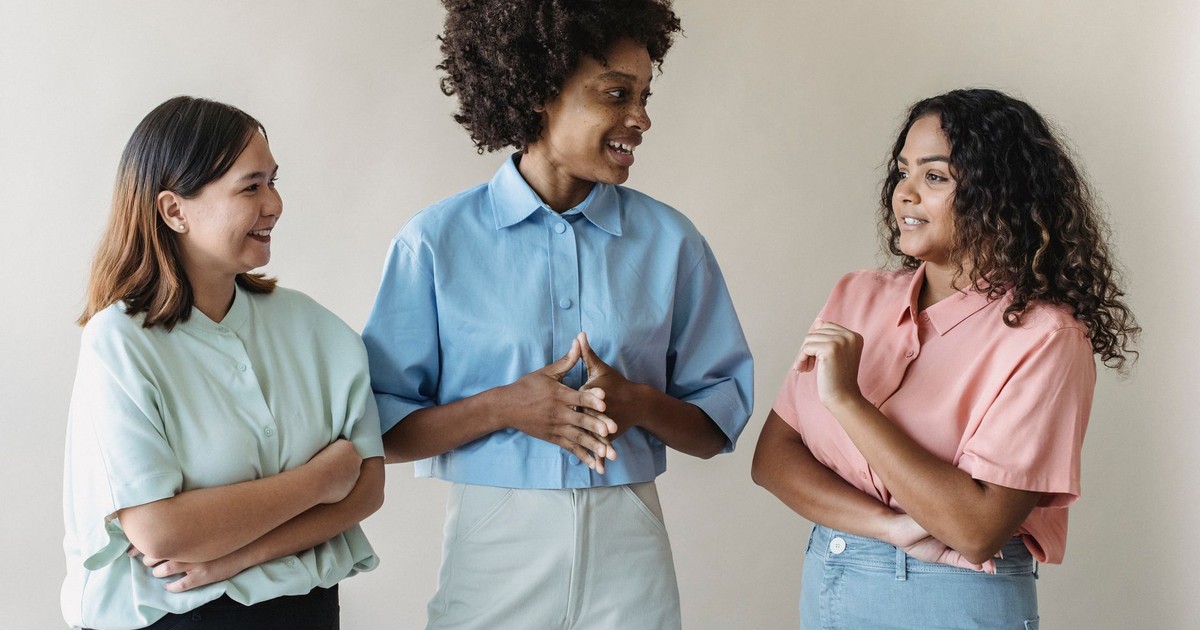 Group of diverse women smiling and talking, showcasing casual fashion in an indoor setting.