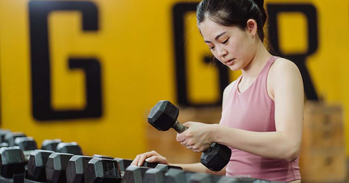 Young woman lifting dumbbell in gym, focusing on strength training with sports equipment.