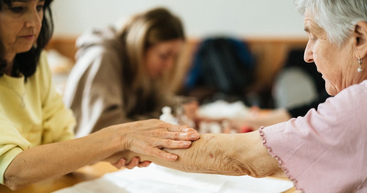 A caregiver gently supports an elderly woman's arm during a community activity.