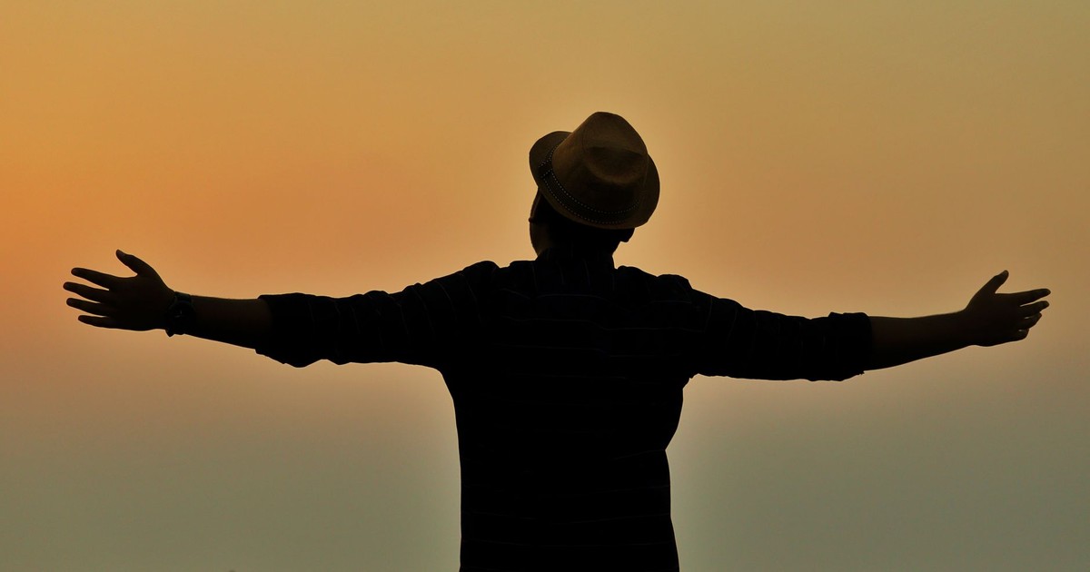 A person in silhouette, wearing a fedora, spreads arms at sunset on a beach in Saint Martin.