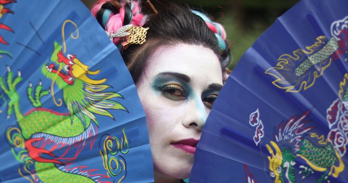 Vibrant portrait featuring a woman with striking makeup holding decorative fans adorned with dragons.