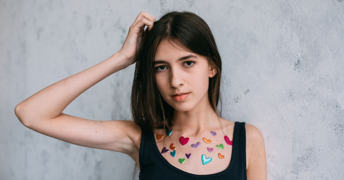 Young woman wearing a black top adorned with colorful heart stickers on her chest.