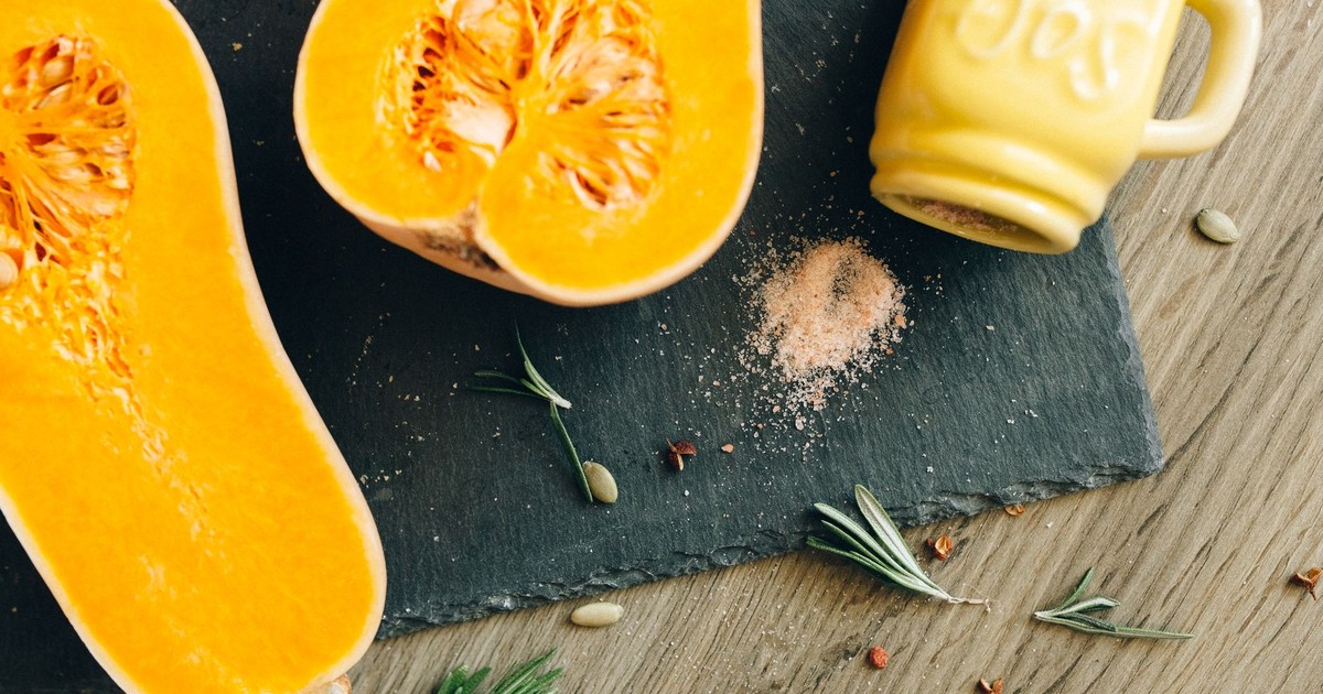 A close-up shot of halved butternut squash with rosemary sprigs and salt on slate.