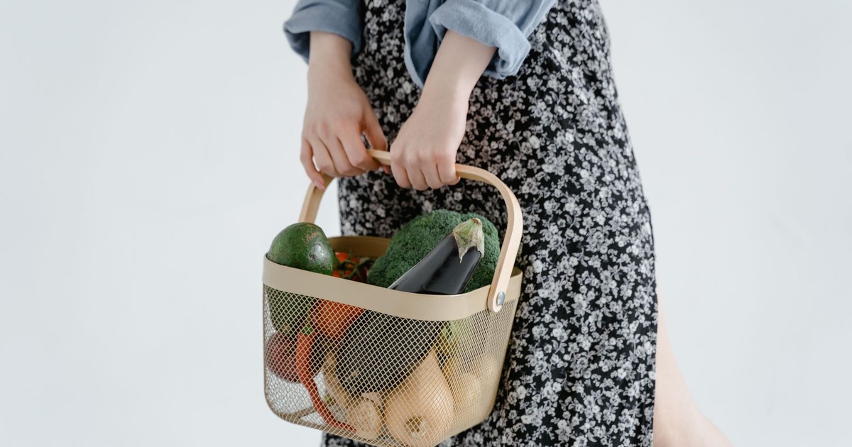 Female holding a basket of fresh vegetables including broccoli and eggplant. Perfect for food and lifestyle themes.