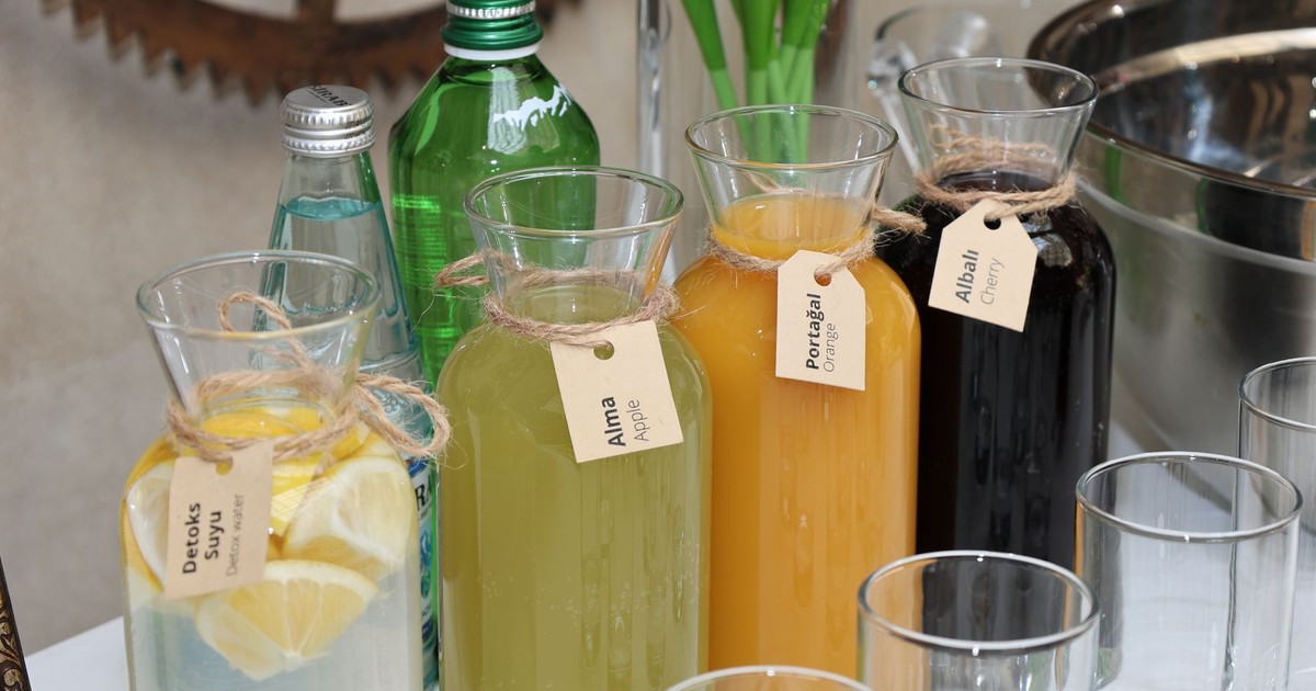 Vibrant assortment of fresh juices in labeled glass bottles with water bottles and glasses arranged outside on a table.