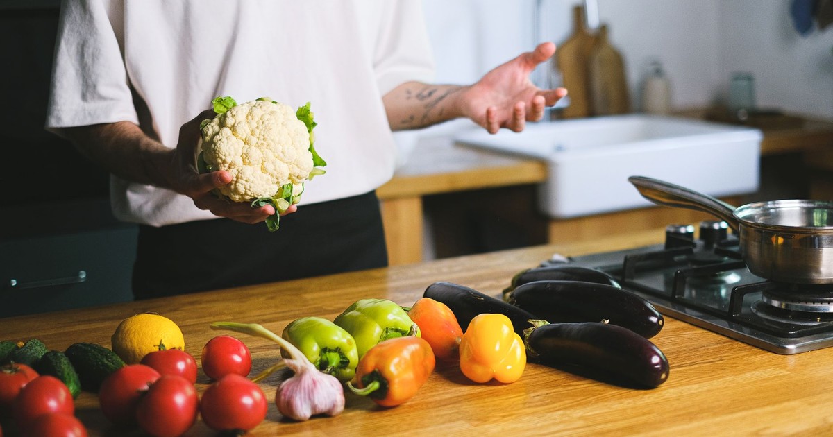 A variety of fresh vegetables including cauliflower, eggplants, and peppers ready for cooking on a kitchen counter.