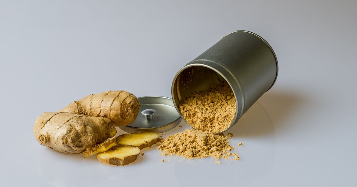 Close-up of fresh ginger root with sliced pieces and ginger powder spilled from a metal container.