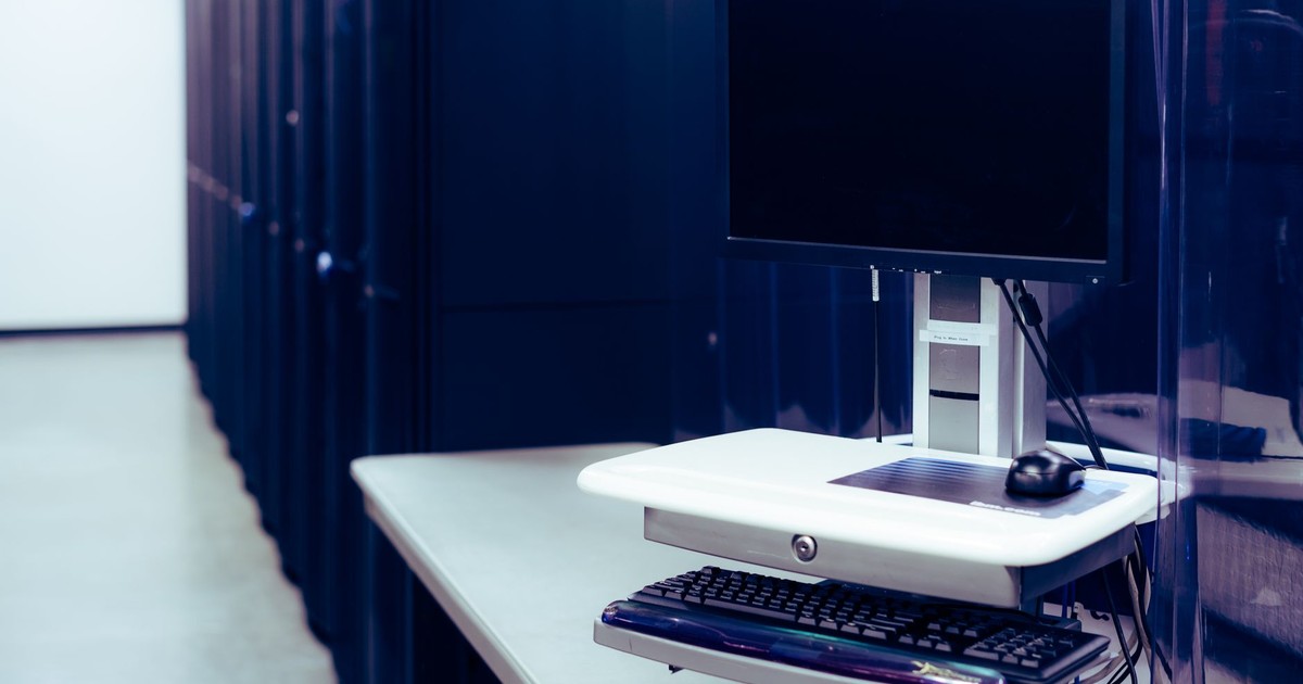 Contemporary computer with black screen placed on stand near row of server steel racks in data center