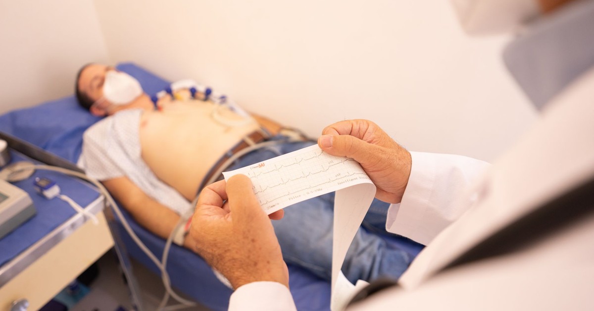 A doctor analyzes an ECG printout while a patient undergoes monitoring in a medical clinic.
