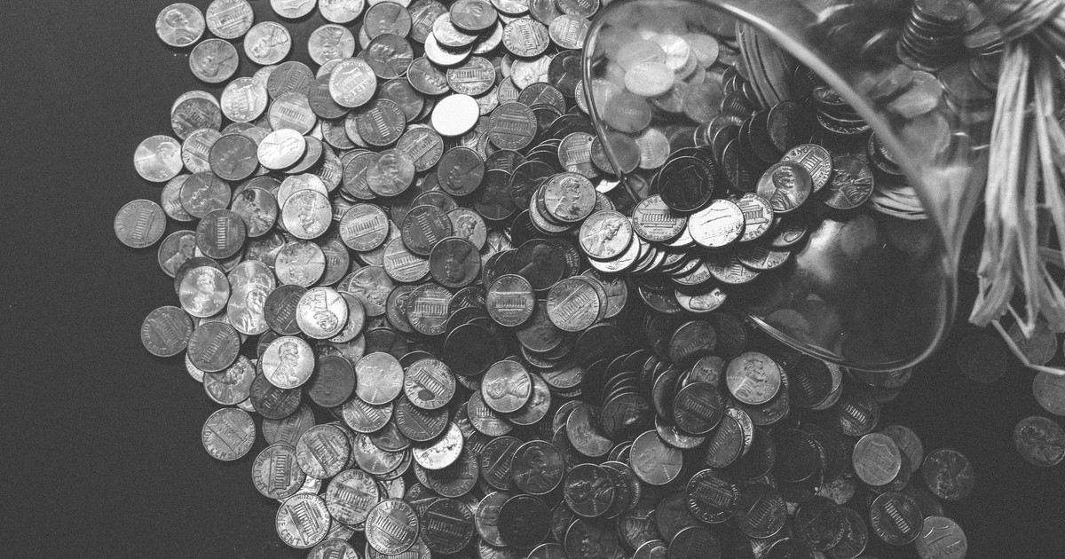 Monochrome image of coins spilling from a glass jar, symbolizing wealth and savings.