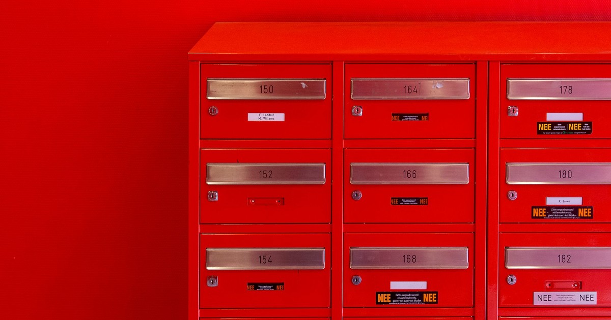 A row of sleek red mailboxes with metallic number panels and keyholes against a red background.