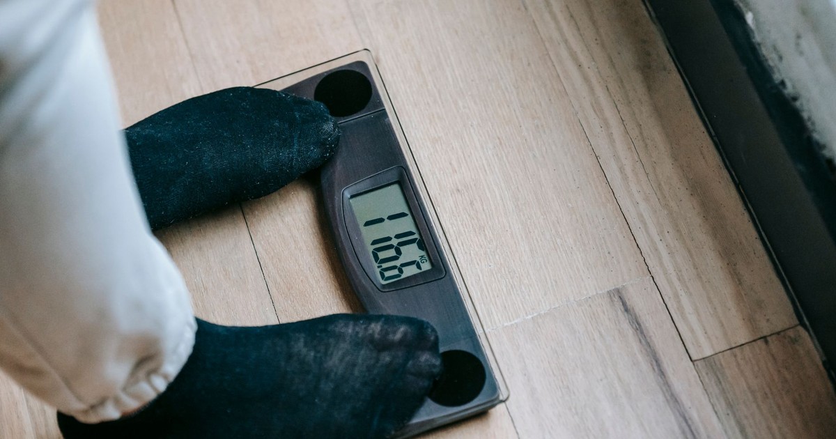 From above of unrecognizable person in socks standing on electronic weighing scales while checking weight on parquet during weight loss