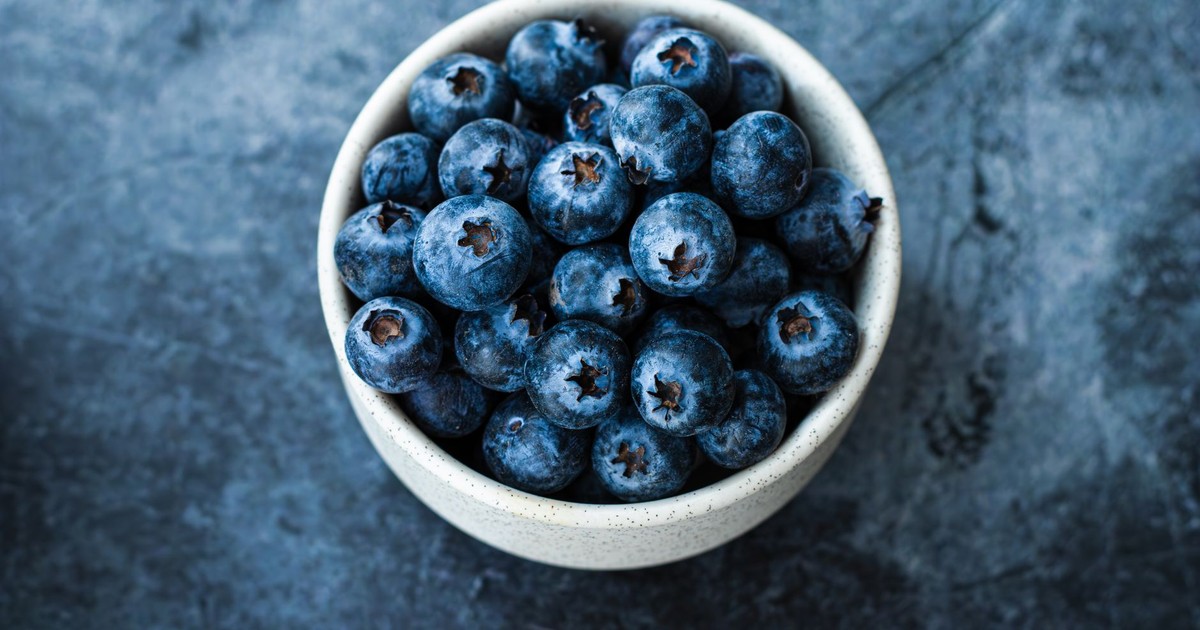 A close-up shot of blueberries in a white bowl on a dark textured background, emphasizing fresh, healthy eating.