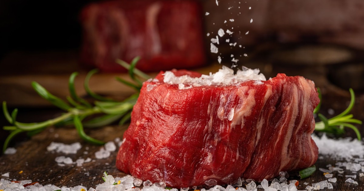 Close-up of raw beef steak with sea salt and herbs on a wooden surface.