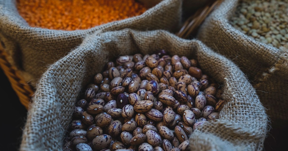 Close-up of pinto beans, lentils, and other grains in burlap sacks in a market setting.