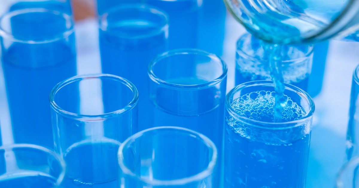 Close-up of blue liquid being poured into glass test tubes in a laboratory setting.