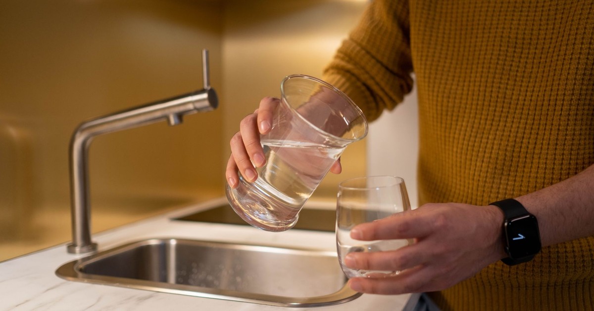 Person pouring water from a pitcher into a glass in a contemporary kitchen setting.