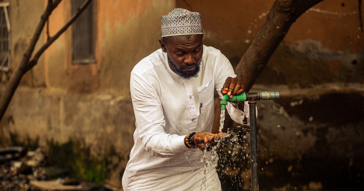 A man washing hands under faucet outdoors in Nigeria, emphasizing hygiene and daily life.