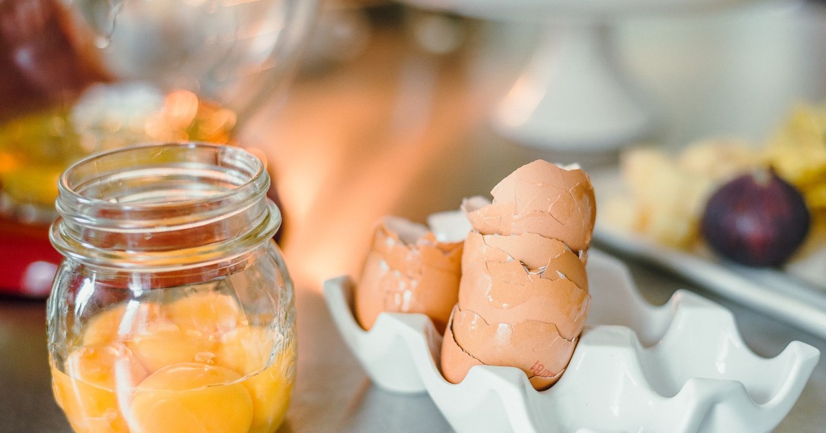 Cracked brown egg shells and yolks in a glass jar on a kitchen counter.