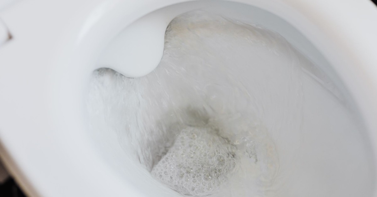 High angle of clean white ceramic toilet bowl with flushing foamy water in bathroom