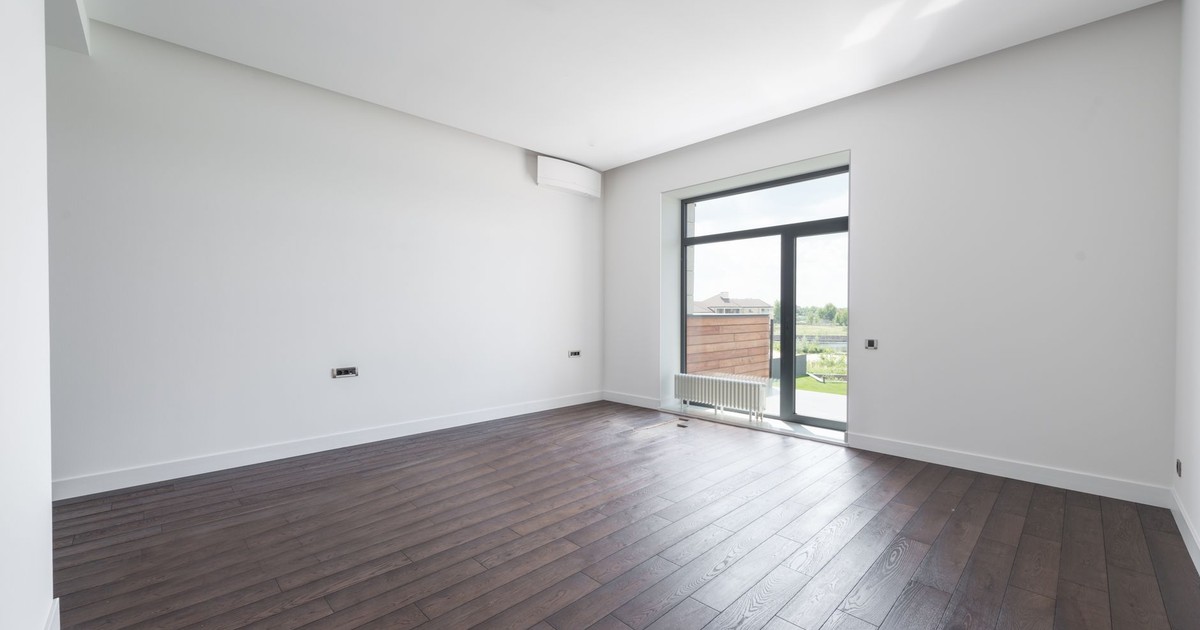 Spacious empty room in new apartment with wooden parquet floor and white wall on sunny day
