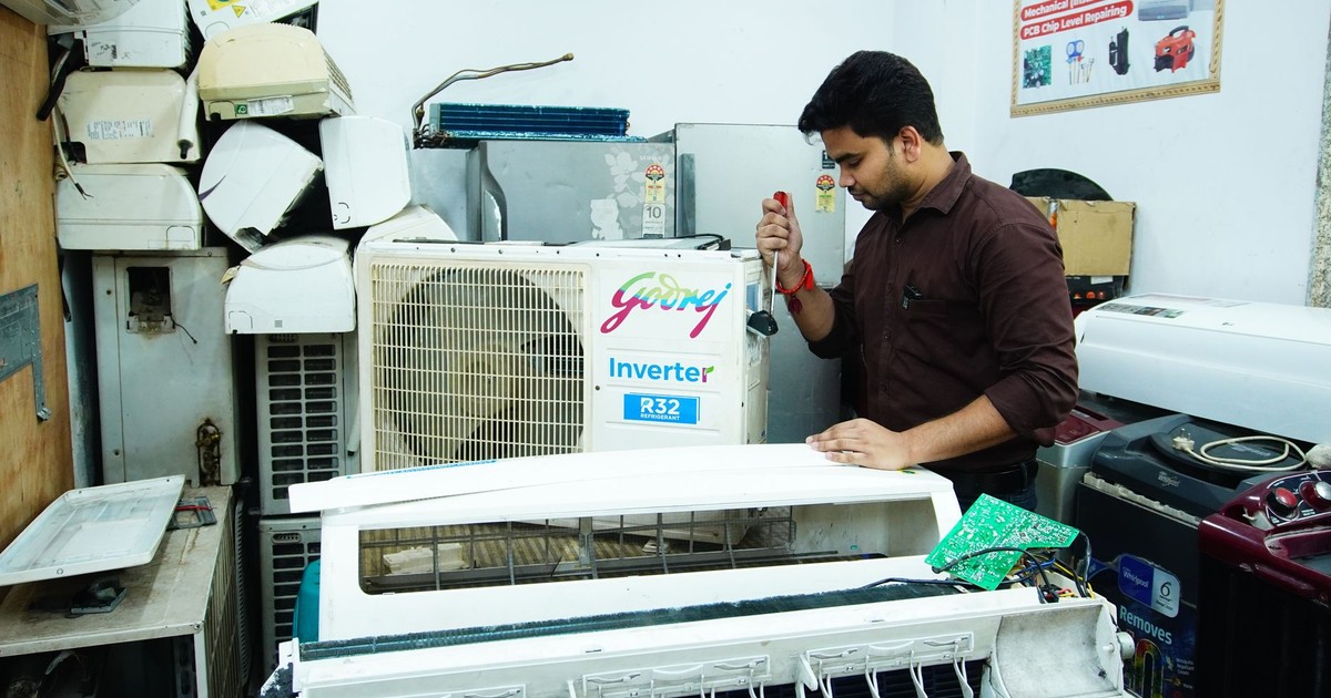 Technician repairing an air conditioner unit in New Delhi workshop.