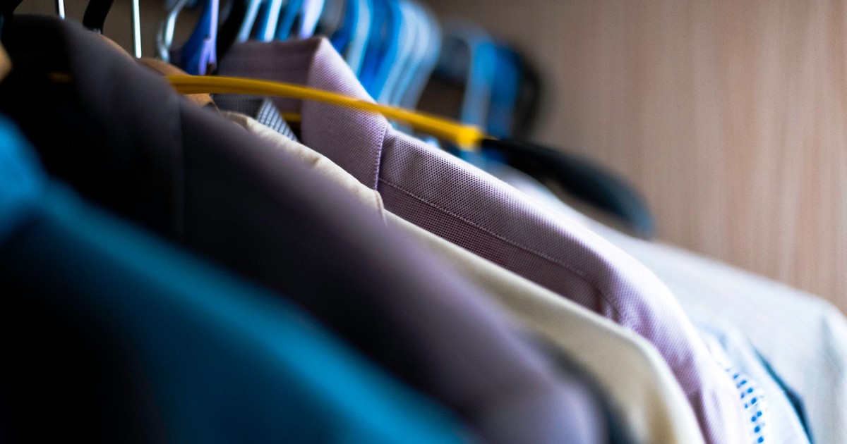 Close-up of various shirts hanging on colorful hangers inside a wardrobe.