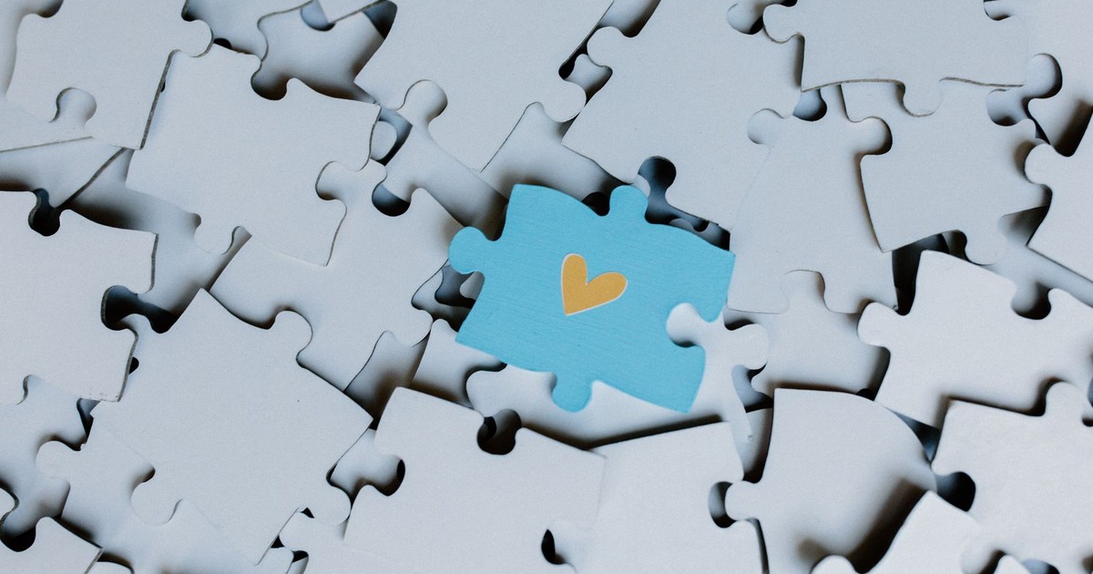A standout blue puzzle piece with a heart symbol among white puzzle pieces, showing uniqueness.