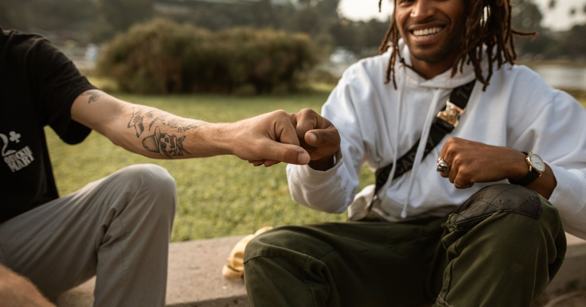 Two friends enjoying a sunny day, sitting in a park, exchanging a friendly fist bump.