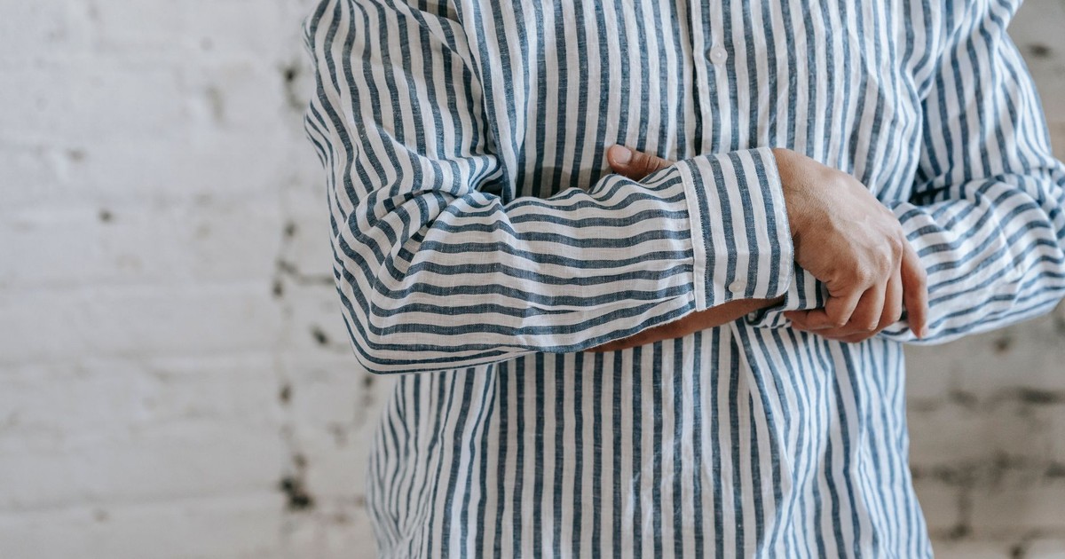 A person standing indoors with hands folded, wearing a blue and white striped shirt.