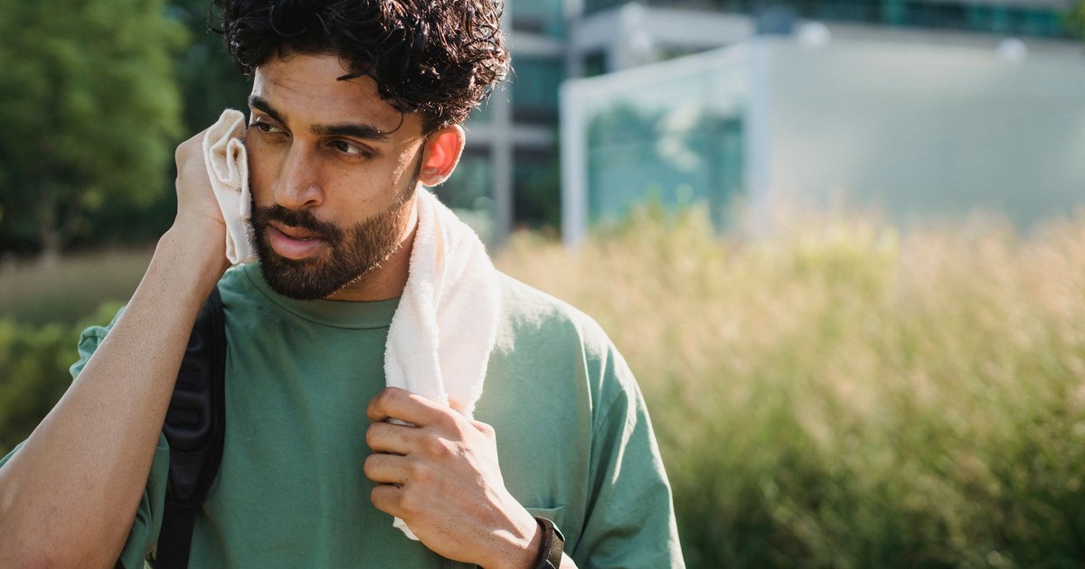 Man taking a break from exercise, using a towel to cool down outdoors on a sunny day.