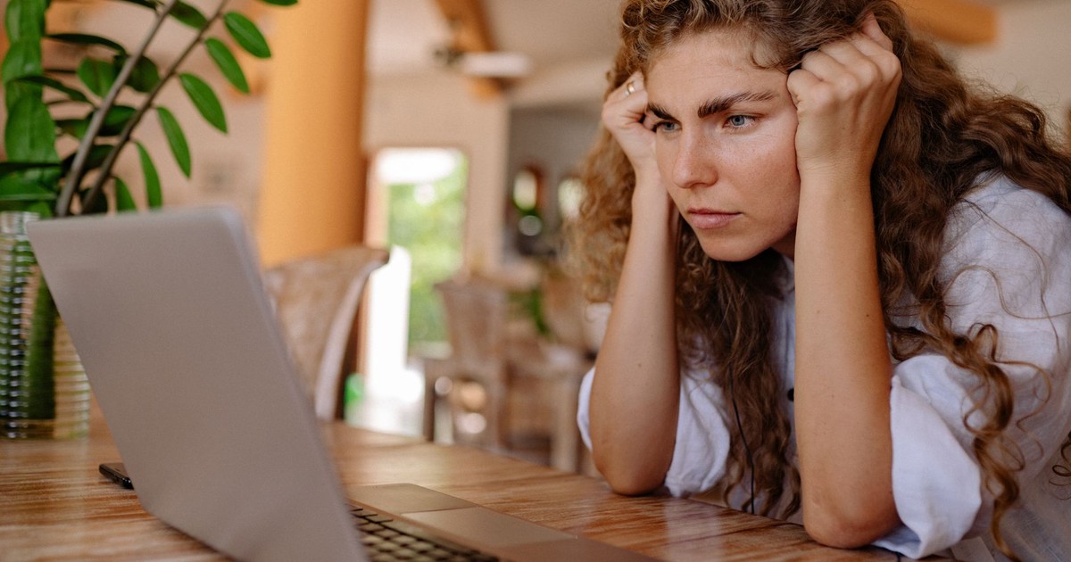 A woman with curly hair intensely focusing on her laptop indoors with plants and natural lighting.