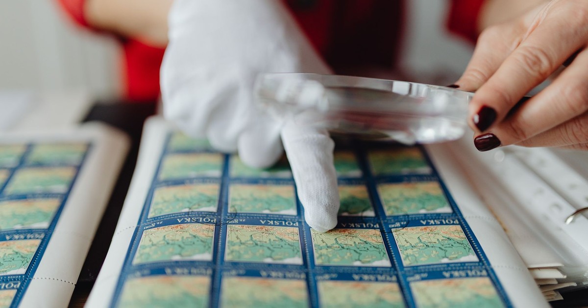 Close-up of a person inspecting vintage stamps with a magnifying glass and gloves.