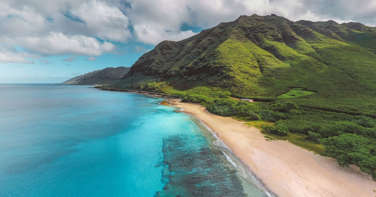 Stunning aerial view of a vibrant Hawaiian coastline with lush mountains and crystal-clear waters.