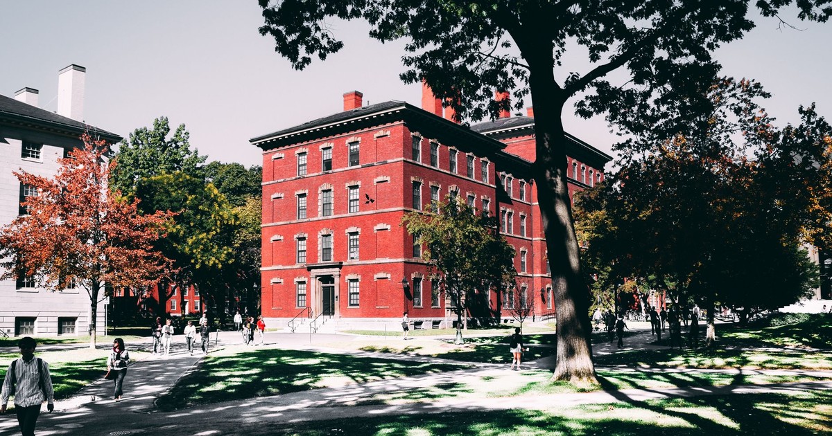 View of a historic red brick university building surrounded by lush trees and walking paths.