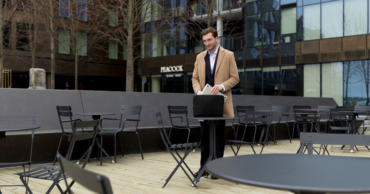 Elegant businessman arranging his briefcase at an outdoor café in a modern urban area.