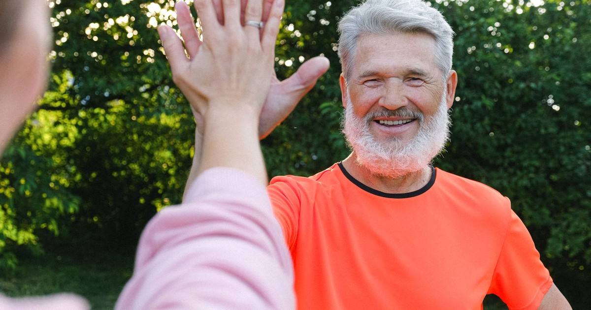 Cheerful aged man in bright clothes smiling and giving high five  to friend in sunny day