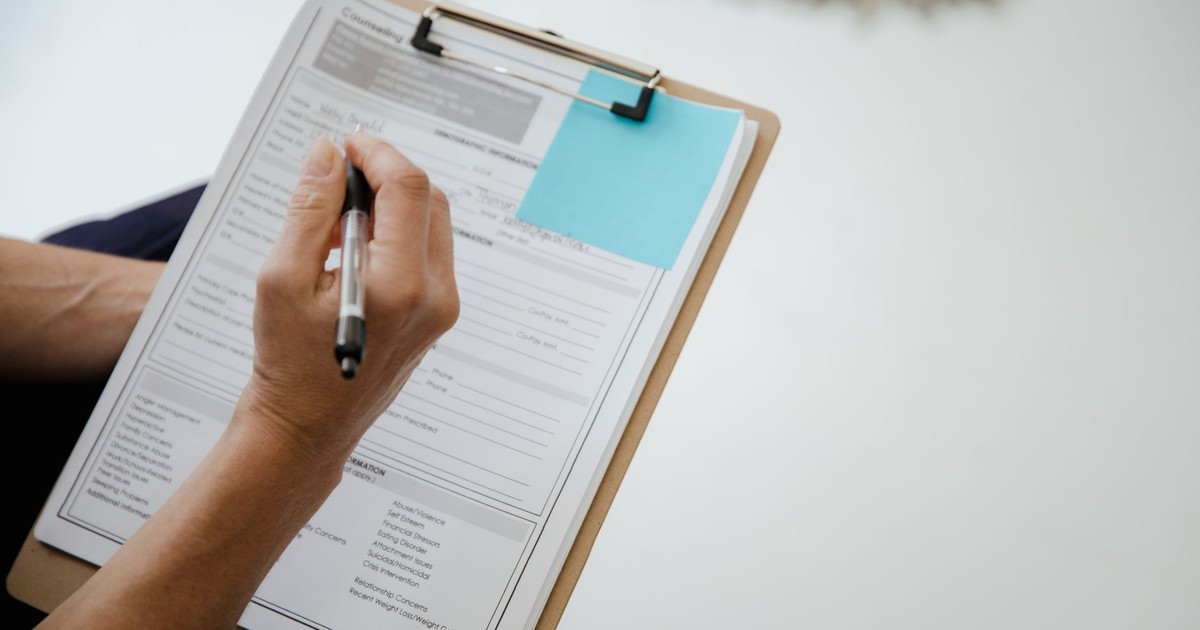A person writes on a document using a clipboard indoors.
