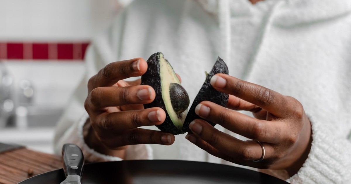 Close-up of hands preparing a fresh avocado in a kitchen setting.