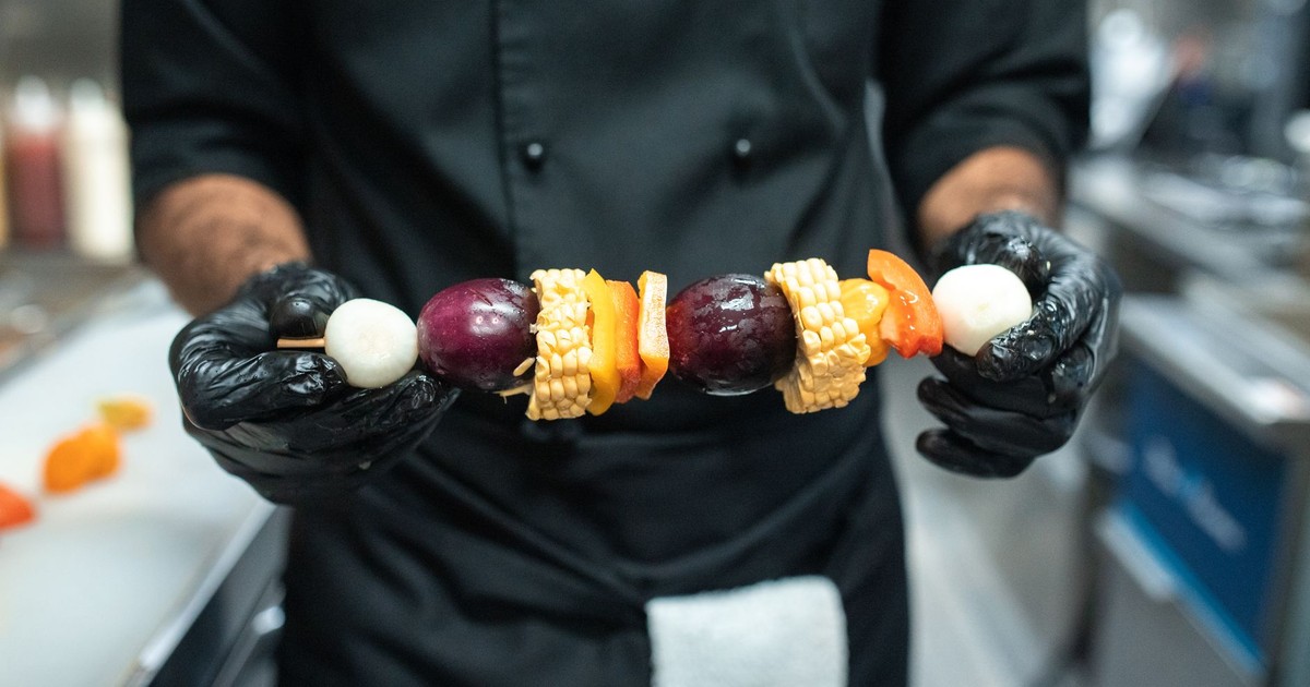 Close-up of chef holding a colorful vegetable skewer in a professional kitchen.