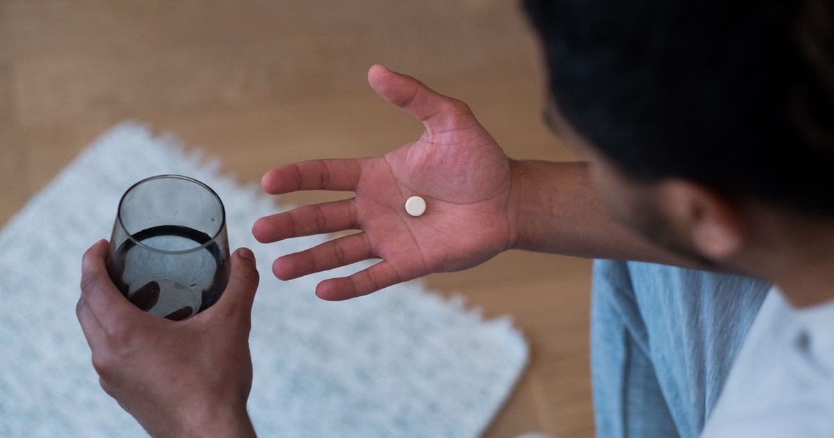 Close-up of a man about to take medication with water, indoors.