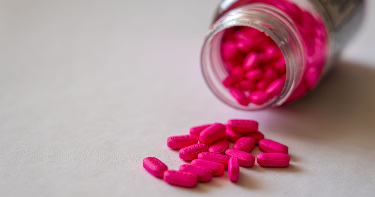 Close-up of an open bottle spilling pink pills onto a surface, indicating medication use.