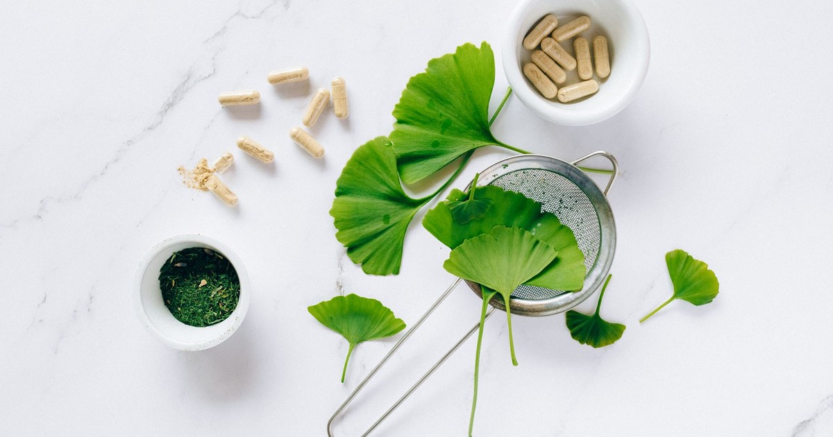 Flat lay of ginkgo leaves, capsules, and herbal powder on marble for natural health remedy.