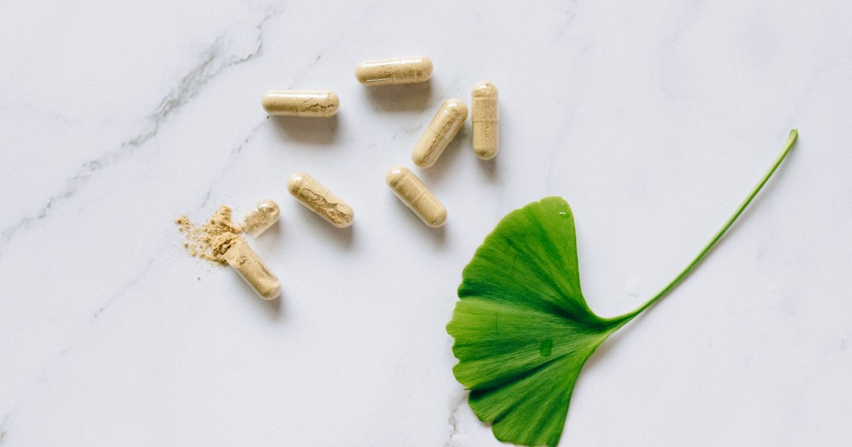 Top view of Ginkgo Biloba capsules with a leaf on a marble surface, symbolizing natural supplements.