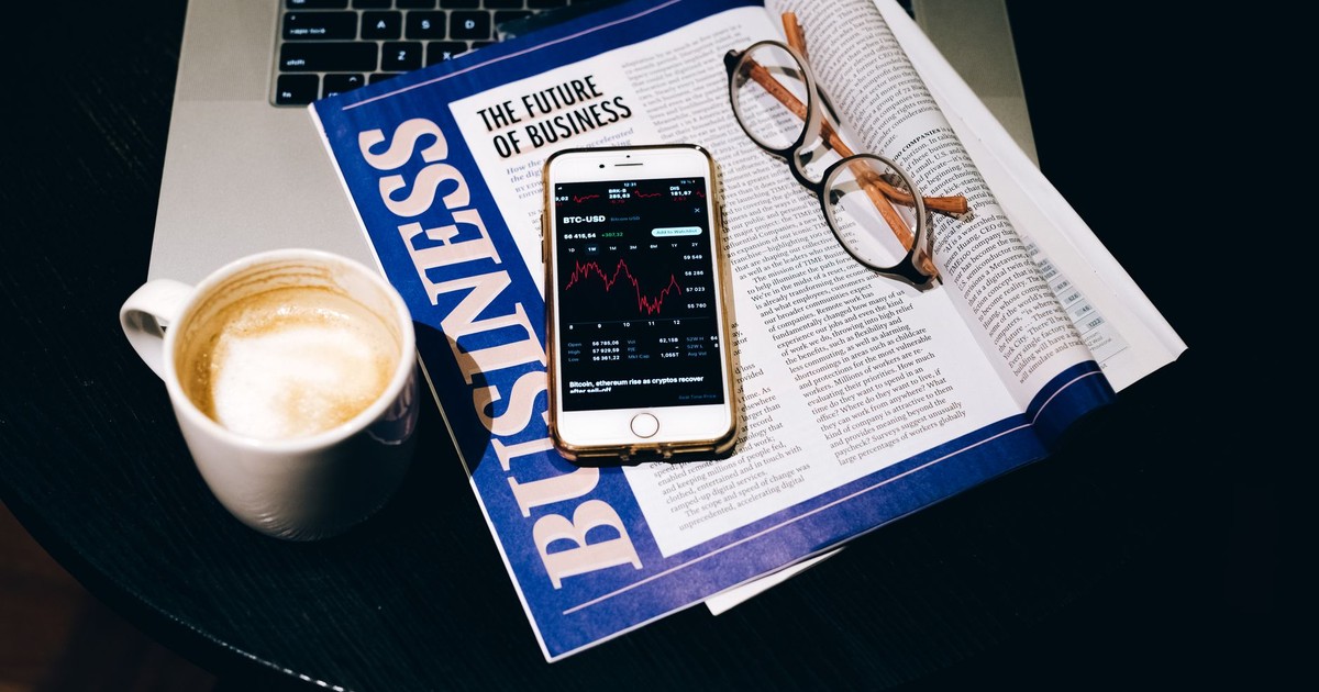 A business setup with a laptop, coffee, phone, and newspaper. Perfect for finance themes.