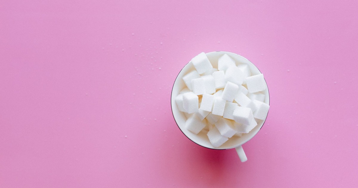 Top view of a cup filled with sugar cubes on a vibrant pink background.