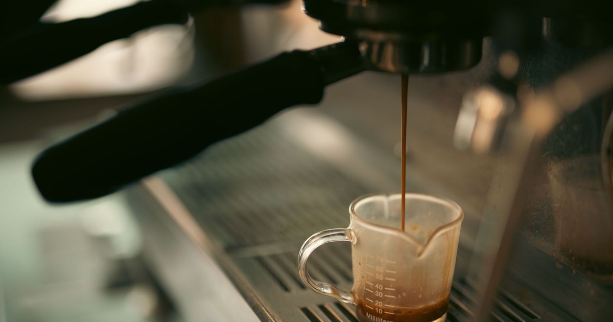 Espresso pouring into a measuring cup from a coffee machine, warm tones.