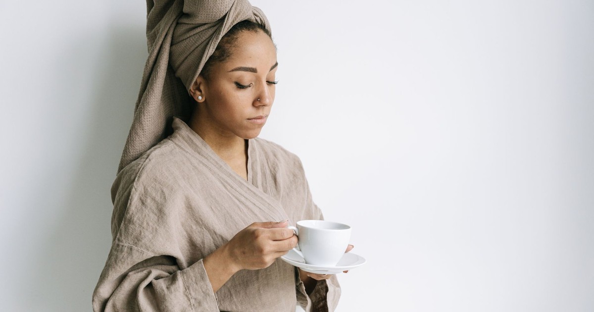 Serene woman in a bathrobe with a towel wrapped around her head, sipping coffee.